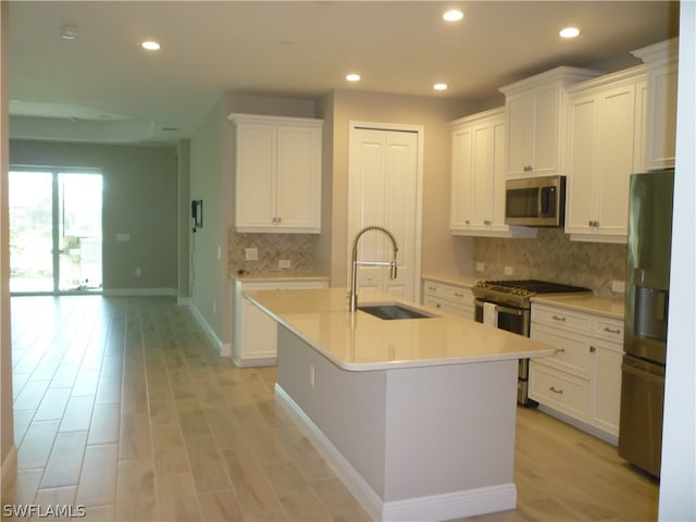 kitchen with tasteful backsplash, an island with sink, stainless steel appliances, sink, and white cabinetry