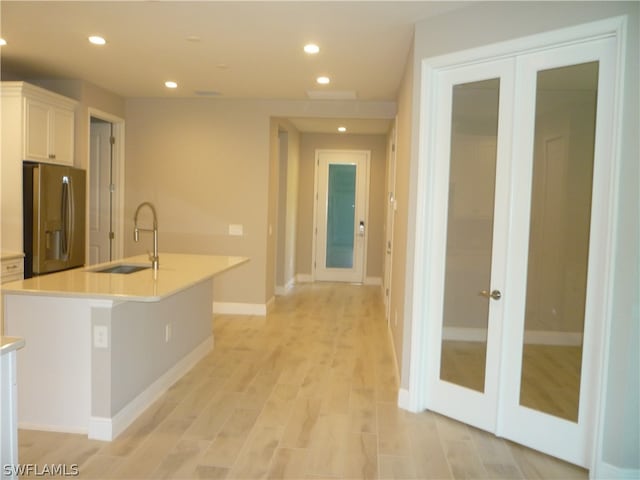 kitchen with light hardwood / wood-style floors, french doors, an island with sink, stainless steel fridge with ice dispenser, and sink