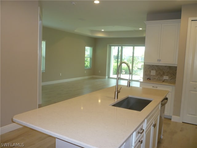 kitchen with light hardwood / wood-style floors, white cabinets, a center island with sink, backsplash, and sink