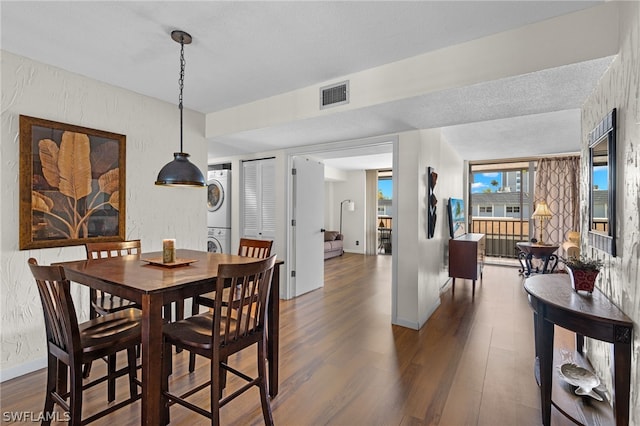 dining area featuring a textured ceiling, dark hardwood / wood-style floors, and stacked washer and clothes dryer