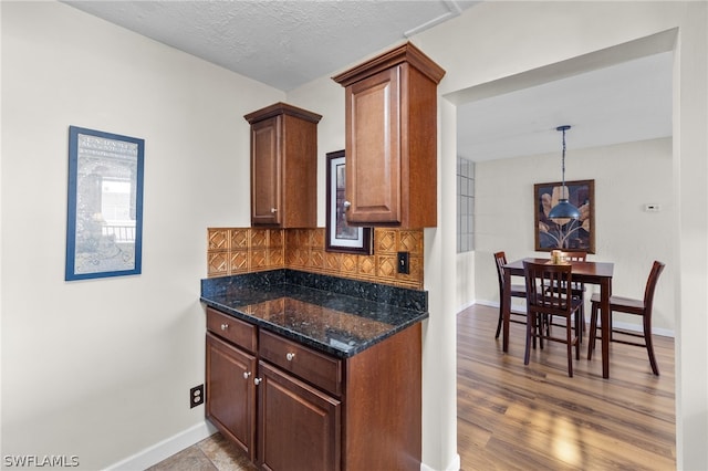 kitchen featuring a textured ceiling, dark stone countertops, hanging light fixtures, and tasteful backsplash