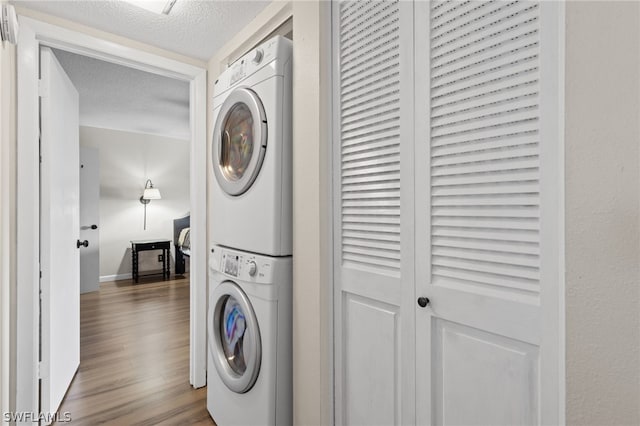 laundry room with hardwood / wood-style flooring, a textured ceiling, and stacked washer and clothes dryer