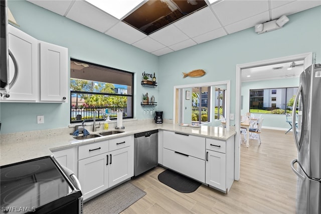 kitchen with kitchen peninsula, appliances with stainless steel finishes, light stone countertops, sink, and white cabinetry