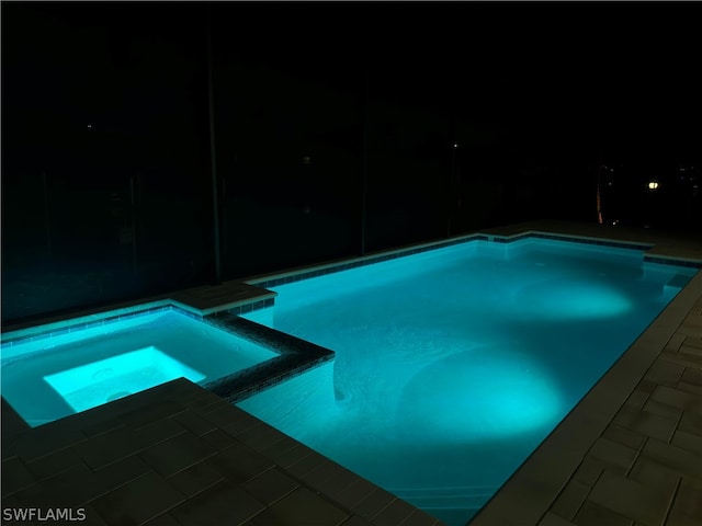 pool at night featuring an in ground hot tub