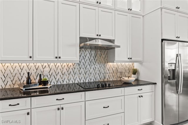 kitchen featuring backsplash, dark stone counters, stainless steel fridge, black electric cooktop, and white cabinetry