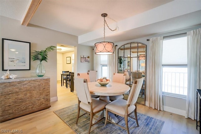 dining room featuring light wood-type flooring, a wealth of natural light, and beamed ceiling