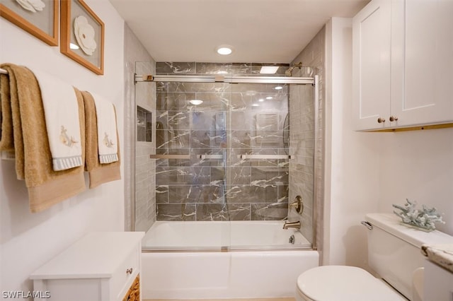 bathroom featuring toilet and bath / shower combo with glass door