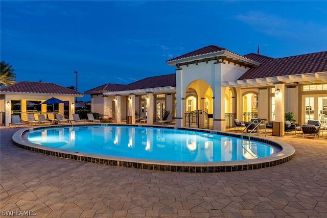 pool at night featuring a patio area