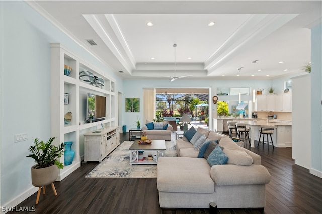 living room with crown molding, a tray ceiling, and dark wood-type flooring