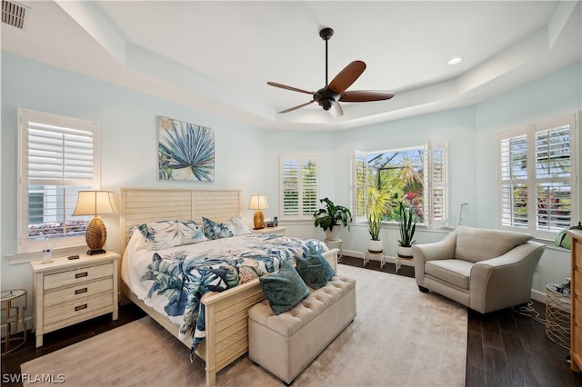 bedroom featuring ceiling fan, a raised ceiling, multiple windows, and dark wood-type flooring