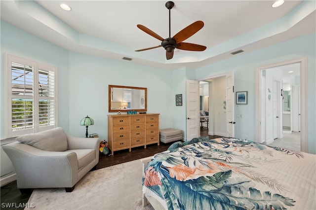 bedroom with dark hardwood / wood-style floors, a raised ceiling, ceiling fan, and connected bathroom