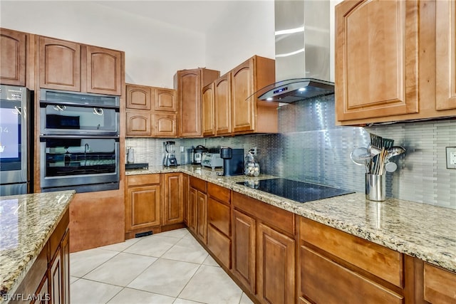 kitchen featuring light stone counters, wall chimney exhaust hood, double oven, tasteful backsplash, and black electric stovetop