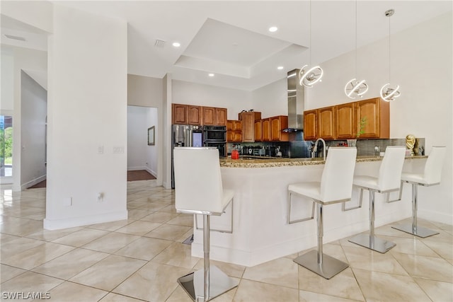 kitchen featuring decorative light fixtures, backsplash, a raised ceiling, a breakfast bar area, and range hood