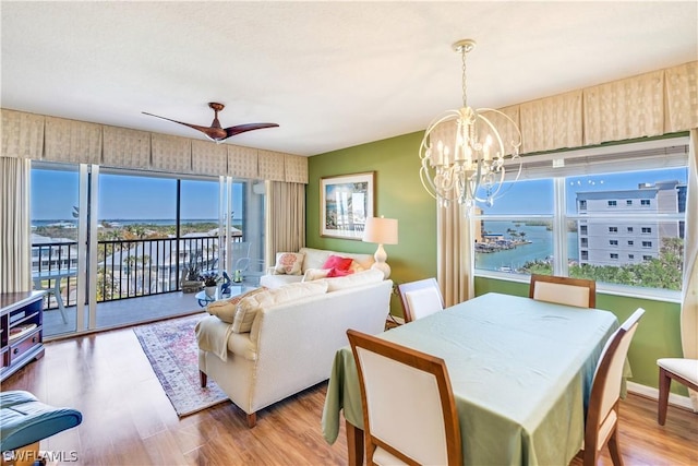 dining area featuring a water view, ceiling fan with notable chandelier, and light wood-type flooring