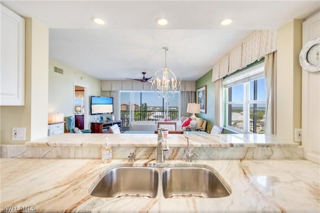 kitchen featuring light stone countertops, an inviting chandelier, hanging light fixtures, and sink