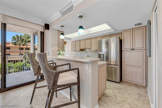 kitchen with hanging light fixtures, light brown cabinetry, stainless steel fridge, tasteful backsplash, and a kitchen bar