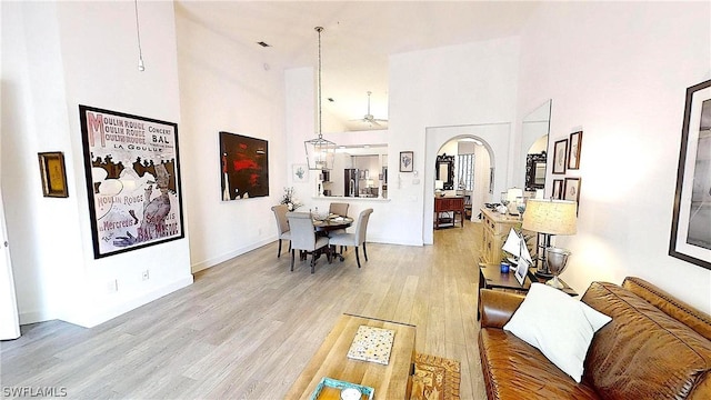 dining room with arched walkways, a towering ceiling, and light wood finished floors