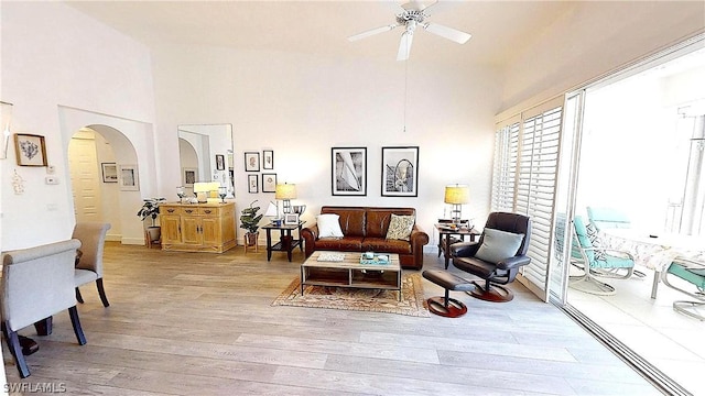 sitting room with arched walkways, a high ceiling, a ceiling fan, and light wood-style floors