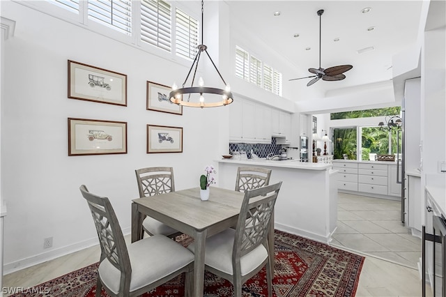 dining room with ceiling fan with notable chandelier, light tile floors, and a towering ceiling