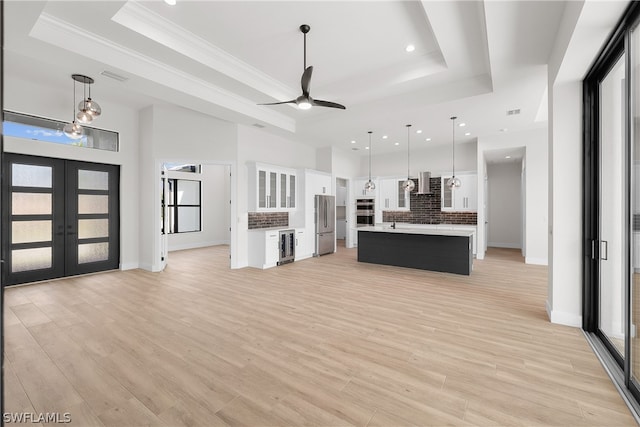 unfurnished living room featuring french doors, light hardwood / wood-style floors, and a tray ceiling