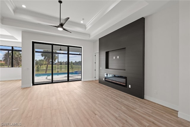 unfurnished living room featuring ceiling fan, light hardwood / wood-style floors, a fireplace, a raised ceiling, and ornamental molding