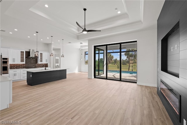 living room featuring sink, light hardwood / wood-style floors, ceiling fan, and a tray ceiling