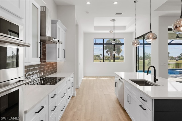 kitchen featuring sink, tasteful backsplash, a raised ceiling, wall chimney range hood, and pendant lighting