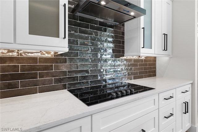 kitchen featuring tasteful backsplash, black electric cooktop, wall chimney range hood, and light stone counters