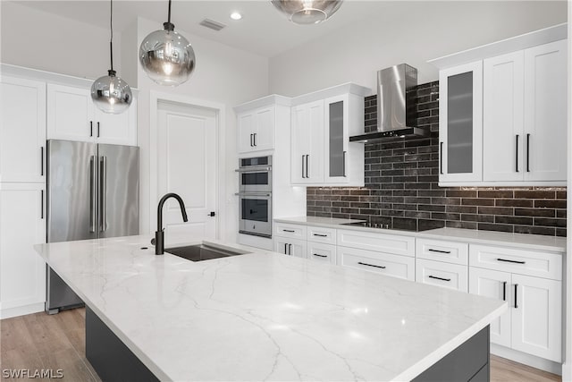 kitchen featuring decorative light fixtures, backsplash, appliances with stainless steel finishes, wall chimney range hood, and sink