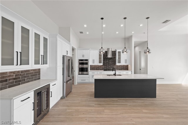 kitchen featuring pendant lighting, beverage cooler, backsplash, wall chimney range hood, and an island with sink