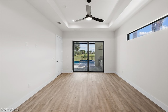 unfurnished room with light hardwood / wood-style flooring, ceiling fan, and a tray ceiling