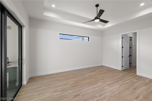 spare room featuring ceiling fan, a raised ceiling, and light wood-type flooring