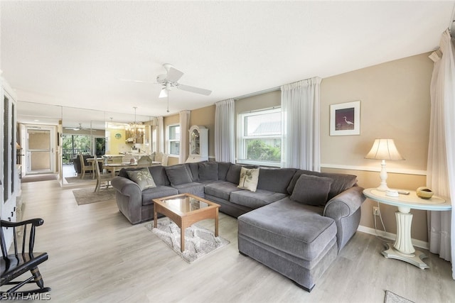 living room with ceiling fan with notable chandelier and light hardwood / wood-style flooring