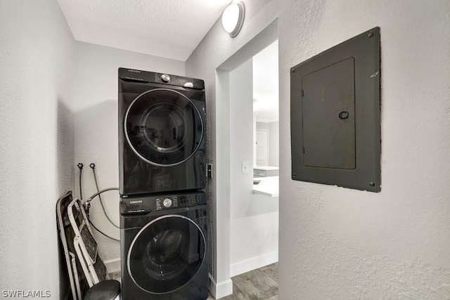 clothes washing area featuring hardwood / wood-style floors, a textured ceiling, electric panel, and stacked washer and clothes dryer