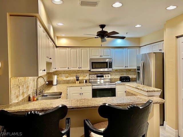 kitchen with white cabinets, ceiling fan, a kitchen bar, and stainless steel appliances