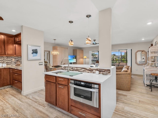 kitchen with pendant lighting, tasteful backsplash, light hardwood / wood-style flooring, oven, and an inviting chandelier