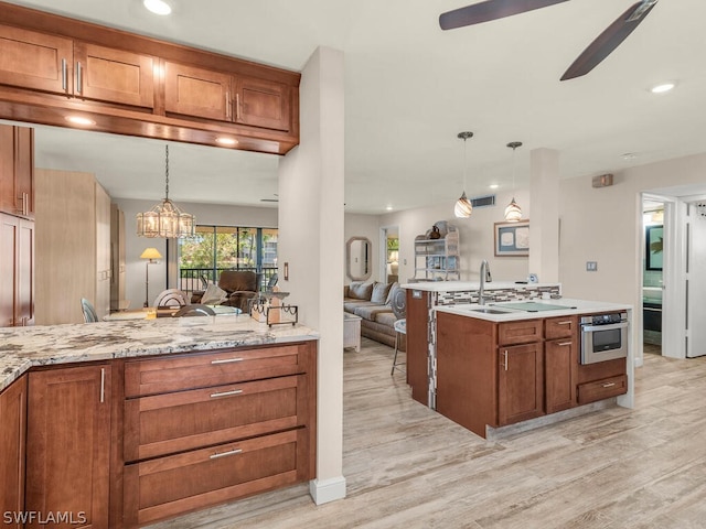 kitchen featuring decorative light fixtures, ceiling fan with notable chandelier, light stone counters, and light hardwood / wood-style floors