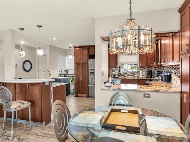 kitchen with hanging light fixtures, backsplash, light hardwood / wood-style floors, kitchen peninsula, and stainless steel refrigerator with ice dispenser