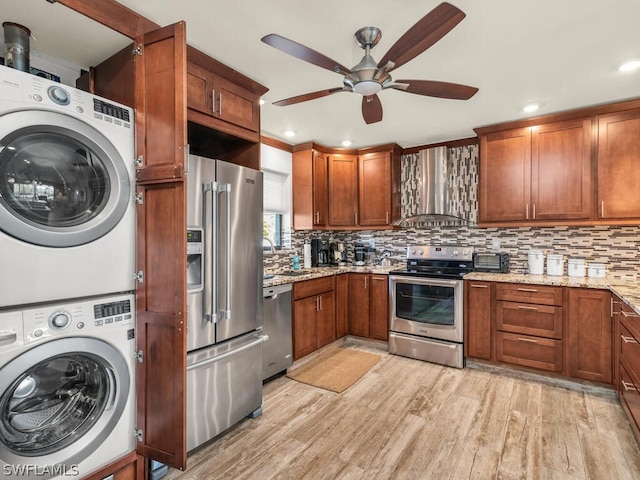 kitchen featuring stainless steel appliances, light hardwood / wood-style flooring, light stone countertops, wall chimney exhaust hood, and ceiling fan