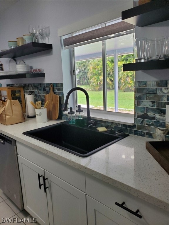 kitchen featuring white cabinets, light stone counters, stainless steel dishwasher, decorative backsplash, and sink