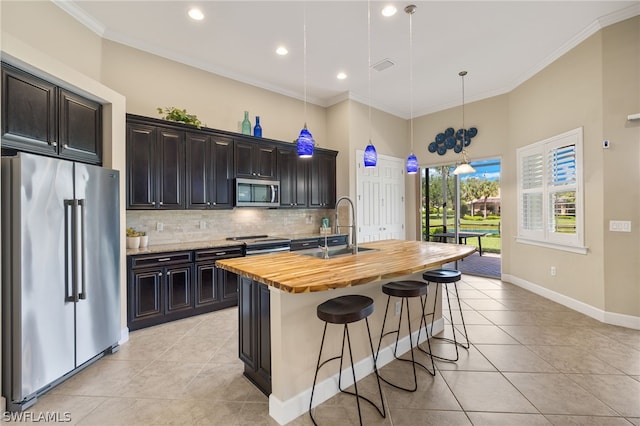 kitchen with butcher block countertops, sink, a kitchen island with sink, stainless steel appliances, and decorative light fixtures