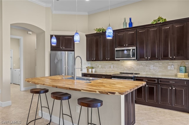 kitchen with appliances with stainless steel finishes, butcher block counters, sink, hanging light fixtures, and a center island with sink