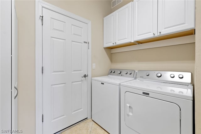 clothes washing area with cabinets, light tile patterned floors, and washer and dryer