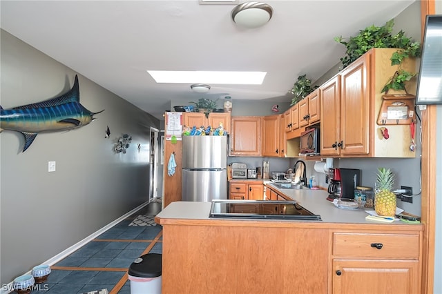 kitchen with a skylight, cooktop, sink, stainless steel fridge, and tile floors