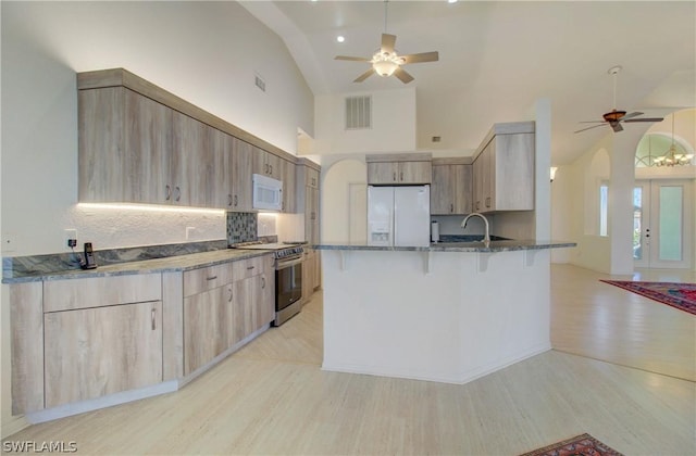 kitchen featuring a kitchen bar, decorative backsplash, white appliances, ceiling fan, and stone countertops