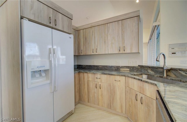 kitchen with light brown cabinetry, stainless steel dishwasher, white fridge with ice dispenser, and dark stone countertops