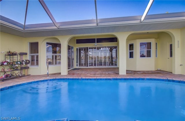 view of swimming pool featuring glass enclosure, ceiling fan, and a patio area