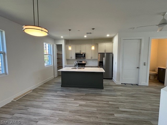 kitchen featuring a center island with sink, appliances with stainless steel finishes, wood finished floors, light countertops, and a sink