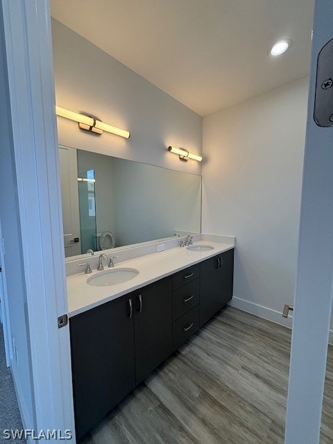 full bath featuring double vanity, wood finished floors, a sink, and a shower with shower door