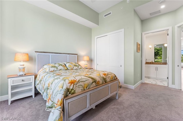 bedroom featuring ensuite bath, light colored carpet, and a closet